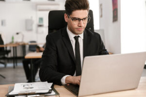 photo-concentrated-businessman-eyeglasses-working-with-documents-laptop-while-sitting-desk-open-plan-office - Galeria laptopów